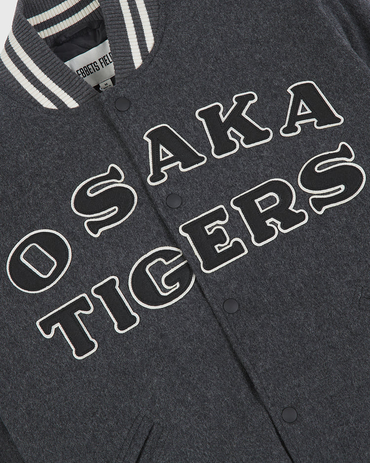 A dark gray Osaka Tigers All-Wool Varsity Jacket by Ebbets Field, featuring a classic white and black striped collar. Bold, outlined “OSAKA TIGERS” lettering stands out on the front, making it a standout addition for collectors of Japanese baseball memorabilia.