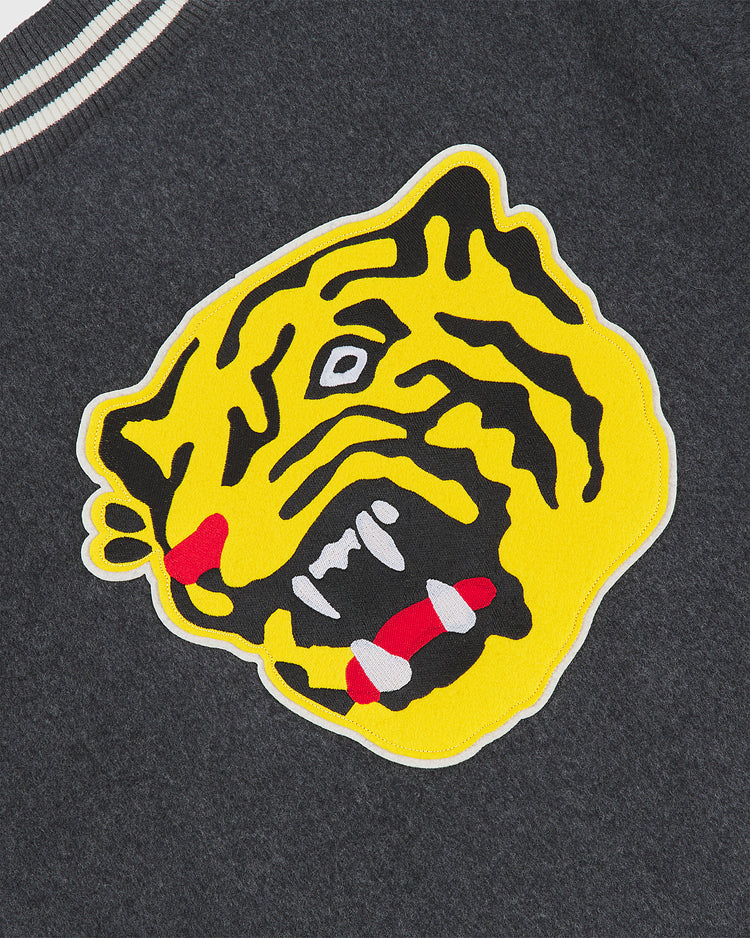 A yellow tiger head patch with red and white accents is sewn onto dark gray wool fabric, echoing classic Japanese baseball memorabilia. Featuring black stripes, bold outlines, and a fierce expression, the patch makes this Ebbets Field Osaka Tigers All-Wool Varsity Jacket an ideal piece for collectors or fans of authentic varsity jackets.