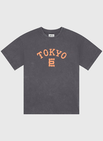 The Ebbets Field Tokyo Giants Pigment-Dyed Short Sleeve Graphic T-Shirt features a gray, pigment-dyed finish and displays bold orange “TOKYO” lettering alongside a stylized E graphic on the front, all inspired by the Tokyo Giants. The shirt is presented against a plain white background.