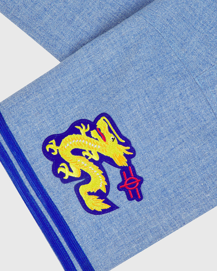 A blue fabric adorned with a yellow dragon in one corner—embroidered as it clutches a red object—and finished with two blue edge stripes, evoking the classic style of the Chunichi Dragons 1969 Authentic Wool Road Jersey by Ebbets Field, meticulously crafted from traditional baseball flannel.