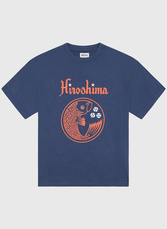 This Ebbets Field Hiroshima Carp Pigment-Dyed Short Sleeve Graphic T-Shirt is a vintage-inspired cotton tee in navy blue, showcasing bold orange “Hiroshima” text above a striking, stylized koi fish and three white flowers arranged in a circular design on the front—a fresh take on classic Hiroshima Carp t-shirt style.
