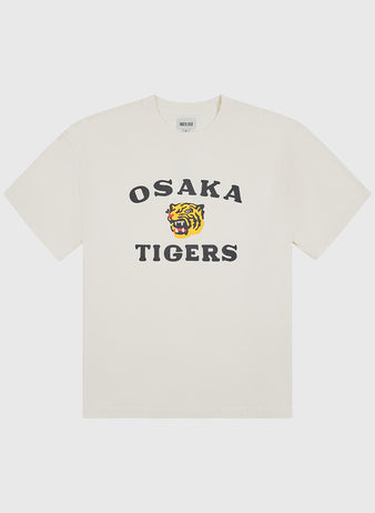 The Ebbets Field Osaka Tigers Short Sleeve Graphic T-Shirt is a white tee designed in vintage baseball style, featuring bold black “OSAKA TIGERS” lettering on the front with a roaring tiger face graphic printed between the words.