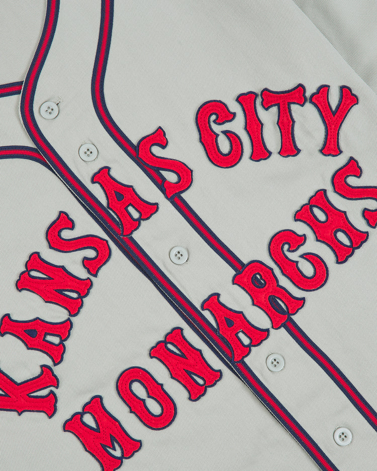 Kansas City Monarchs 1936 Road Jersey Cotton Twill: a gray baseball jersey with red and navy blue striped trim and the red and navy Kansas City Monarchs text appliquéd across the chest.