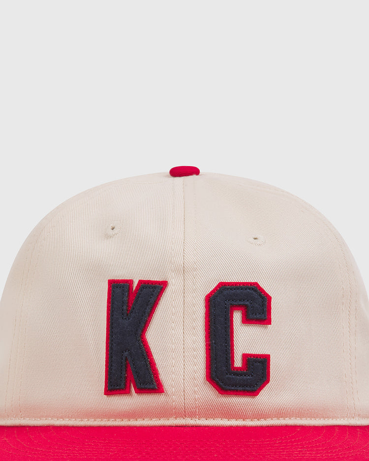 Off-white Kansas City Monarchs 1942 Cotton Twill Ballcap with a red brim, red button top, and navy blue KC lettering with red trim.