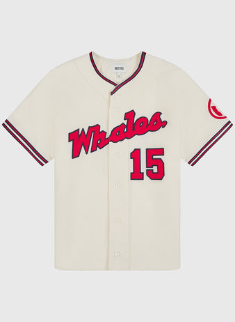 Introducing the Taiyo Whales 1963 Authentic Wool Home Jersey by Ebbets Field—a cream-colored reproduction featuring “Whales.” in bold red script across the chest, number 15 in red, and a distinctive red patch on the left sleeve. This classic wool baseball jersey showcases black trim with front buttons and striking black and red striped accents on the sleeves and collar, capturing the essence of vintage style for devoted fans.