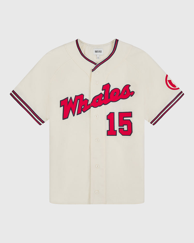 Introducing the Taiyo Whales 1963 Authentic Wool Home Jersey by Ebbets Field—a cream-colored reproduction featuring “Whales.” in bold red script across the chest, number 15 in red, and a distinctive red patch on the left sleeve. This classic wool baseball jersey showcases black trim with front buttons and striking black and red striped accents on the sleeves and collar, capturing the essence of vintage style for devoted fans.