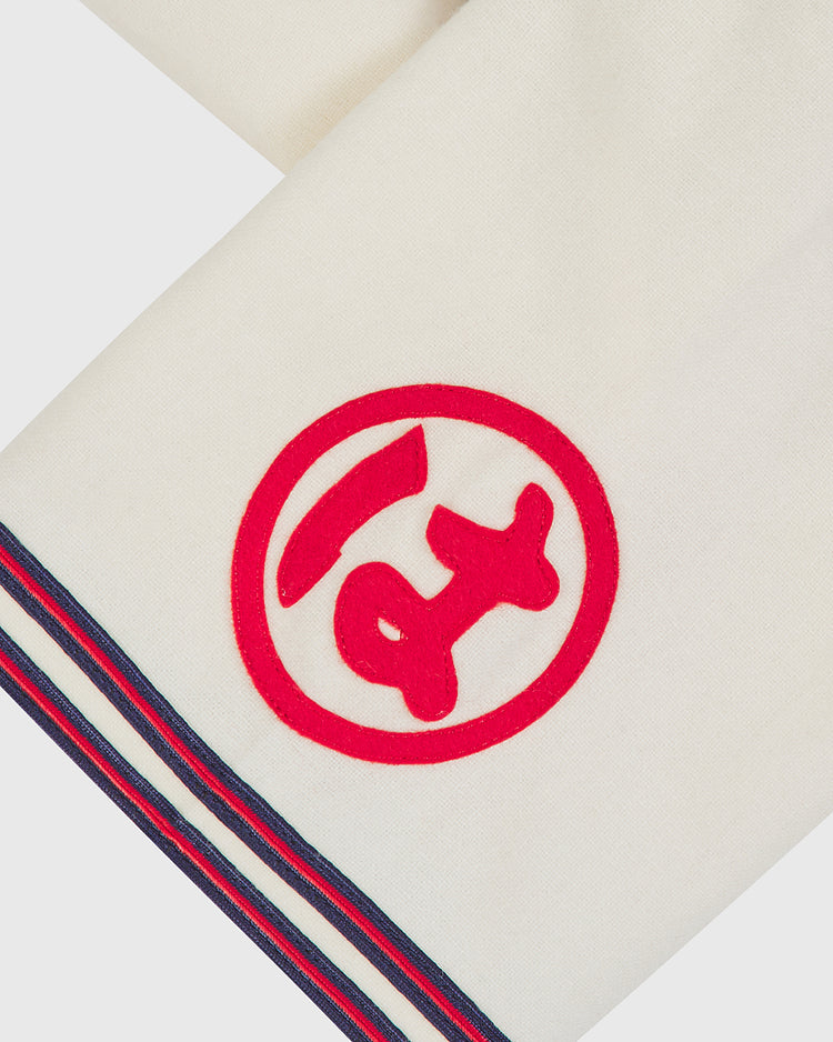 Close-up of a white fabric with blue and red striped trim and a red embroidered symbol resembling a stylized animal inside a circle, evocative of the Taiyo Whales 1963 Authentic Wool Home Jersey by Ebbets Field.