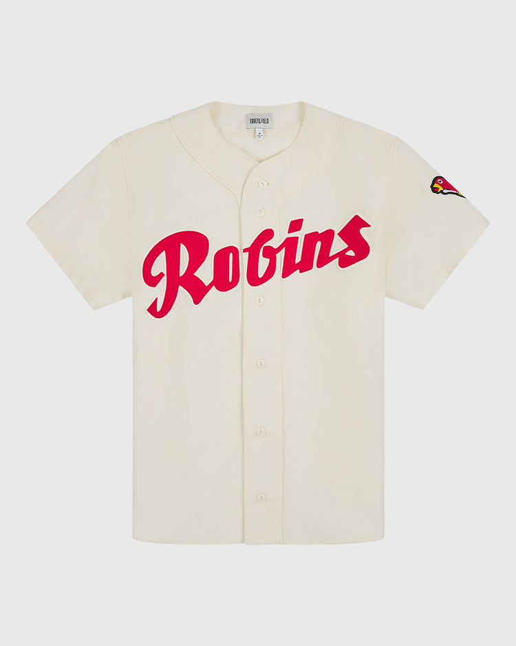 The Ebbets Field Shochiku Robins 1950 Authentic Wool Home Jersey features a cream-colored design with bold red Robins script across the front and a small cardinal bird patch on the left sleeve. Inspired by the iconic 1950 Japanese baseball jersey, this classic piece boasts a traditional button-up front and short sleeves.