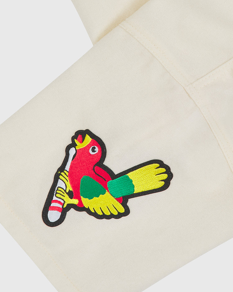 A vibrant embroidered patch depicting a red, yellow, and green bird gripping a baseball bat is stitched onto an off-white wool fabric, echoing the lively motifs of the Shochiku Robins 1950 Authentic Wool Home Jersey by Ebbets Field.