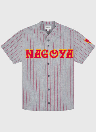 The Ebbets Field Nagoya Club 1938 Authentic Wool Road Jersey showcases a gray short-sleeve design with bold red vertical stripes, black buttons, and “NAGOYA” displayed in prominent red and yellow lettering across the chest. Inspired by the original wool road jersey worn by the 1938 Nagoya Club, this vintage piece also features a striking red graphic on the left sleeve for an extra touch of classic style.