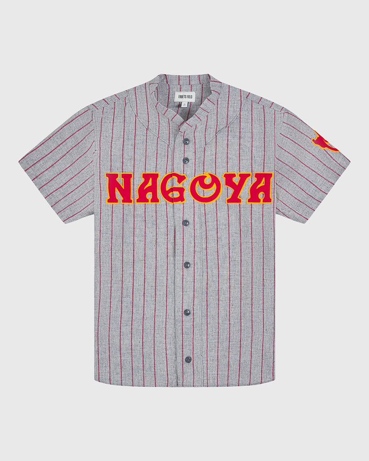 The Ebbets Field Nagoya Club 1938 Authentic Wool Road Jersey showcases a gray short-sleeve design with bold red vertical stripes, black buttons, and “NAGOYA” displayed in prominent red and yellow lettering across the chest. Inspired by the original wool road jersey worn by the 1938 Nagoya Club, this vintage piece also features a striking red graphic on the left sleeve for an extra touch of classic style.