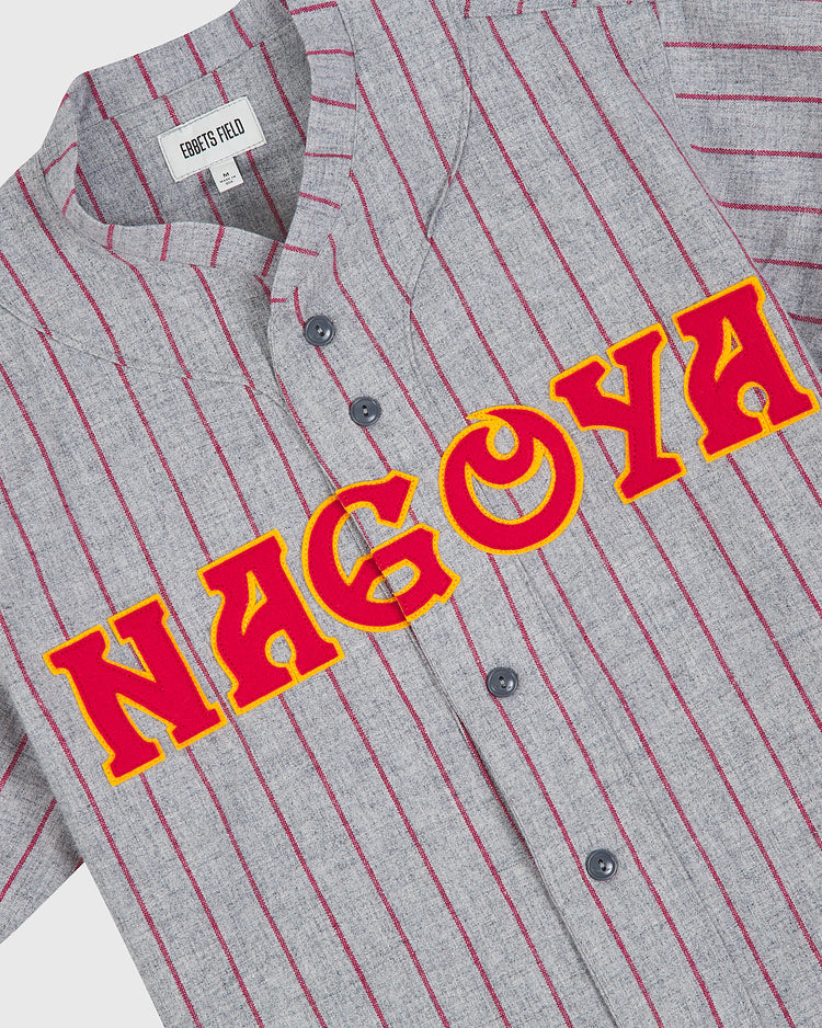 A gray wool road jersey featuring red pinstripes and striking red letters outlined in yellow spelling “NAGOYA” across the chest. Inspired by the 1938 Nagoya Club, this vintage Japanese baseball jersey is an authentic Ebbets Field piece with a visible Ebbets Field label.