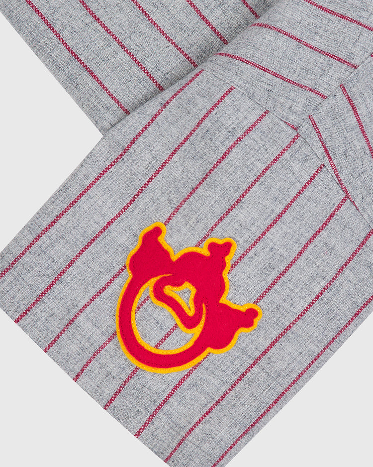 Close-up of a gray wool fabric with thin red stripes and a red and yellow embroidered patch featuring an abstract design, reminiscent of the Ebbets Field Nagoya Club 1938 Authentic Wool Road Jersey—a vintage Japanese baseball jersey.