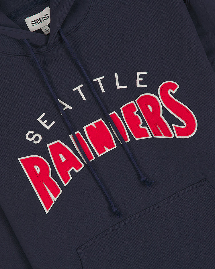 The Seattle Rainiers 1941 Heavyweight Cotton Terry Pullover Hoodie by Ebbets Field is a navy blue, heavyweight pullover featuring SEATTLE RAINIERS in bold white and red lettering across the front, a visible front pocket, and a vintage-inspired tag inside the collar that reads EBBETSFIELD. This design is inspired by the 1941 Seattle Rainiers baseball team.