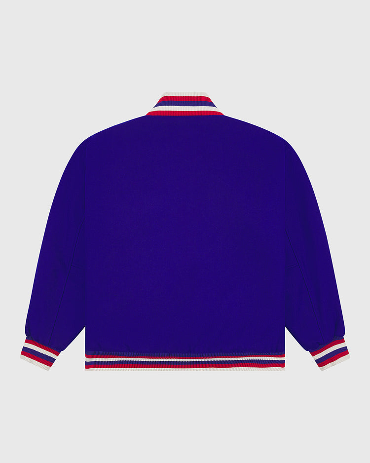 A royal blue Chicago Cubs 1954 Authentic All Wool Varsity Jacket by EFF is displayed from the back, highlighting its red, white, and blue striped cuffs, collar, and waistband against a plain light gray background. This vintage-inspired varsity jacket is a faithful recreation of a classic 1950s Chicago Cubs style.