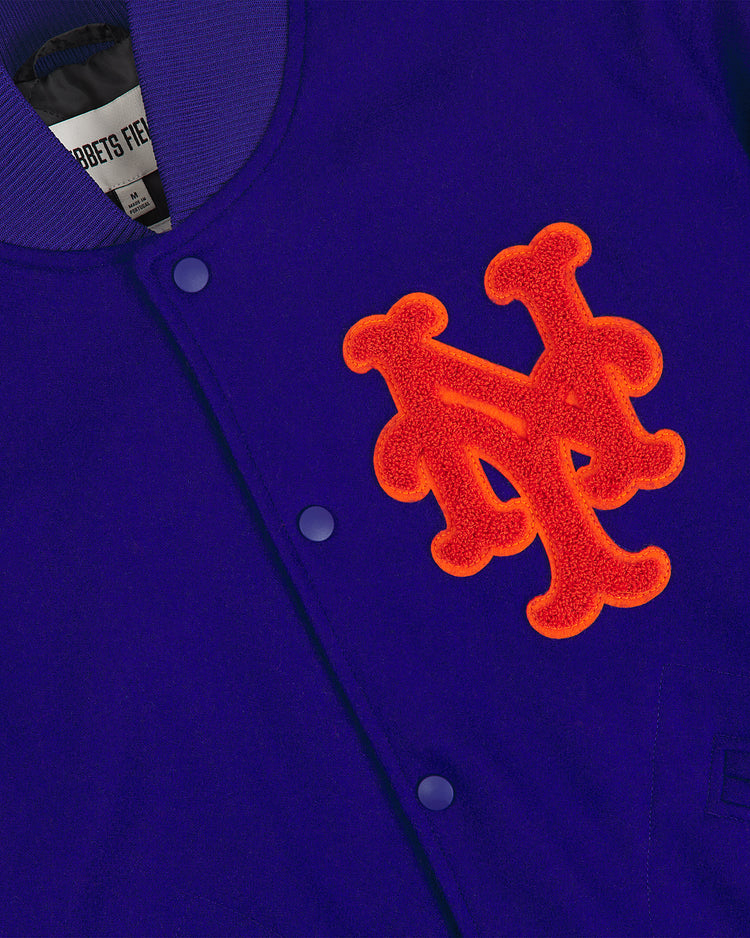 A close-up of the New York Mets 1969 Authentic All Wool Varsity Jacket by EFF, featuring a blue body, purple buttons, and a bold orange NY Mets logo patch on the front. The partially visible tag reads EFF, signifying this is an authentic reproduction of the iconic jacket famously worn by the Miracle Mets.