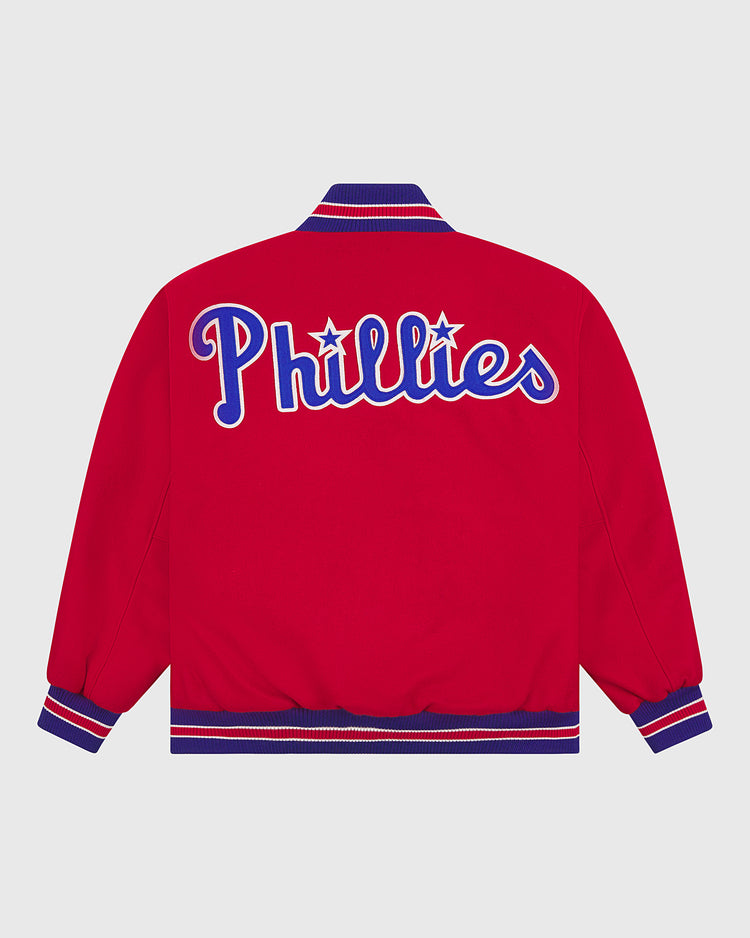 This EFF Philadelphia Phillies 1949 Authentic All Wool Varsity Jacket features a striking red design with blue and white striped cuffs and collar. “Phillies” is emblazoned across the back in large white script outlined in blue, with stars dotting the “i”s—an iconic detail inspired by the original 1949 Phillies team jacket. This officially licensed reproduction captures all the nostalgia of classic baseball history, making it an ideal choice for passionate Phillies fans.