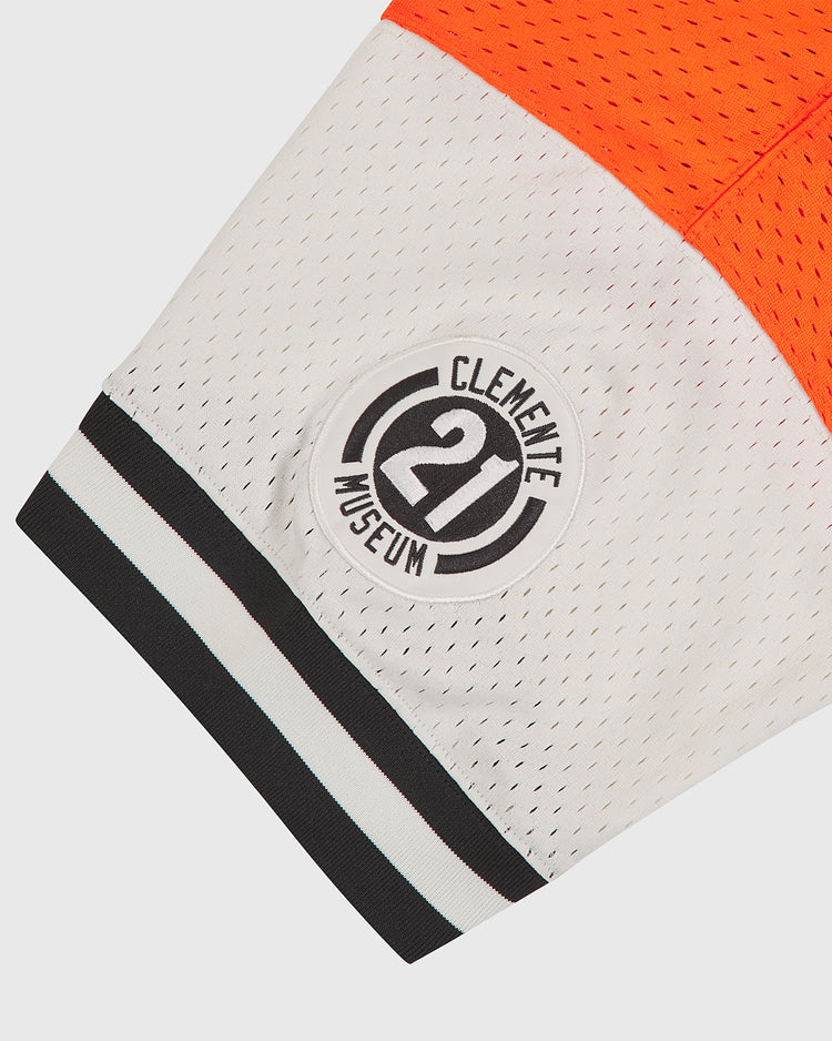 A close-up of the Ebbets Field Clemente Museum x Ebbets Field V-Neck Mesh Jersey sleeve in orange and white mesh, featuring a black and white circular tackle twill appliqué patch that reads “Clemente Museum 21.”.