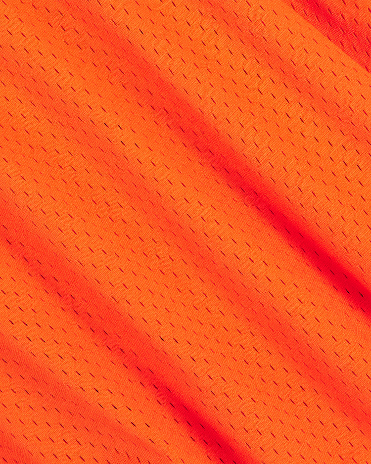 Close-up of orange mesh fabric from The Clemente Museum x Ebbets Field V-Neck Mesh Jersey by Ebbets Field, featuring small, evenly spaced holes and diagonal folds across the surface that evoke the breathable material found in classic Roberto Clemente jerseys with tackle twill appliqué.
