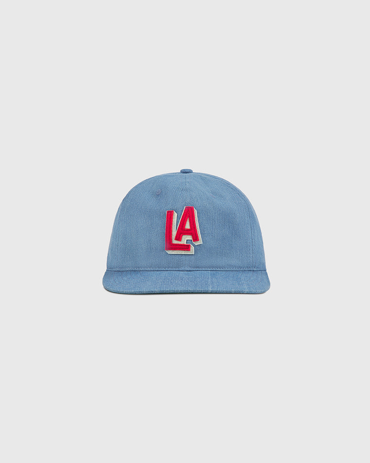 An indigo cotton denim ballcap by Ebbets Field, featuring a striking red and white LA logo on the front inspired by classic PCL history, is displayed against a plain light gray background.