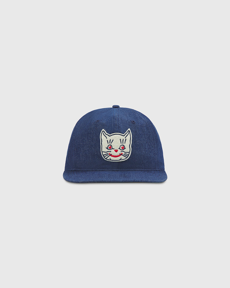 Ebbets Field Kansas City Katz Indigo Cotton Denim Ballcap with a white cartoon cat face patch—red cheeks and a small smile—centered on the front, paying tribute to the iconic Kansas City Katz of Katz Drugstore fame. Shown against a plain, light gray background.