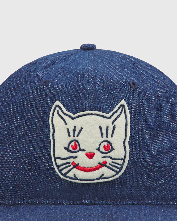 A close-up of the Ebbets Field Kansas City Katz Indigo Cotton Denim Ballcap, showcasing a bold white cat face patch with red eyes, a red nose, and a red smiling mouth embroidered on the front—a playful tribute to the iconic Kansas City Katz design.