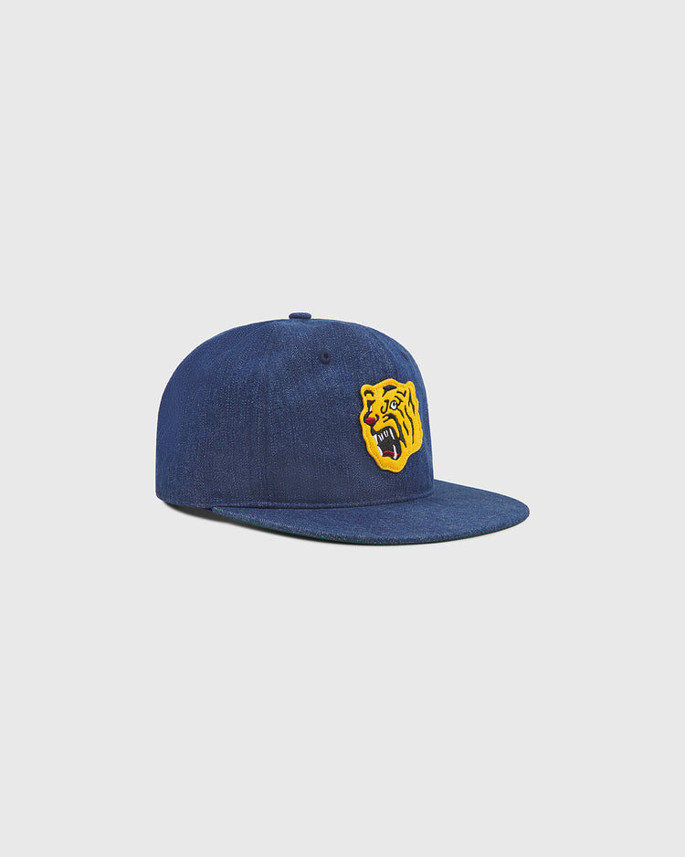 An Osaka Tigers Indigo Cotton Denim Ballcap by Ebbets Field, crafted in blue denim and accented with a yellow patch featuring a roaring bear illustration inspired by the bold spirit of Koshien Field, displayed against a simple light background.