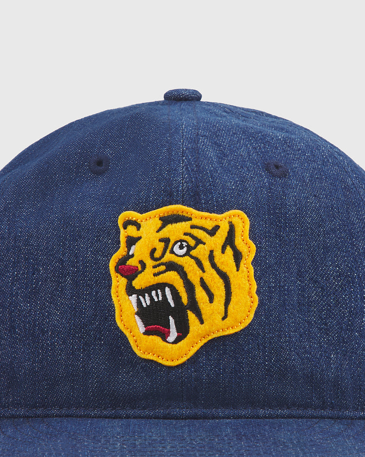 A close-up of the Ebbets Field Osaka Tigers Indigo Cotton Denim Ballcap, showcasing a yellow roaring tiger head patch with black, white, and red details on the front—a bold tribute to the legendary Osaka Tigers and their storied history at Koshien Field.