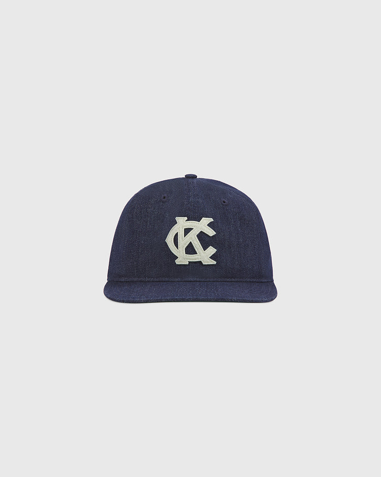 The Kansas City Monarchs Indigo Cotton Denim Ballcap by Ebbets Field features a flat brim and an interlocking KC logo embroidered in white on the front, embracing vintage sports style against a plain light gray background.
