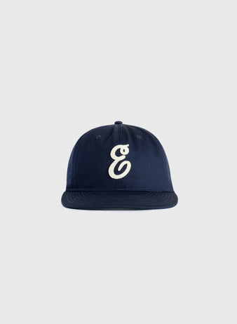 The Ebbets Field Flannels Ebbets Felt E Cotton Twill Ballcap features a navy blue design with a white embroidered E on the front, ideal for everyday wear and shown against a plain light gray background.