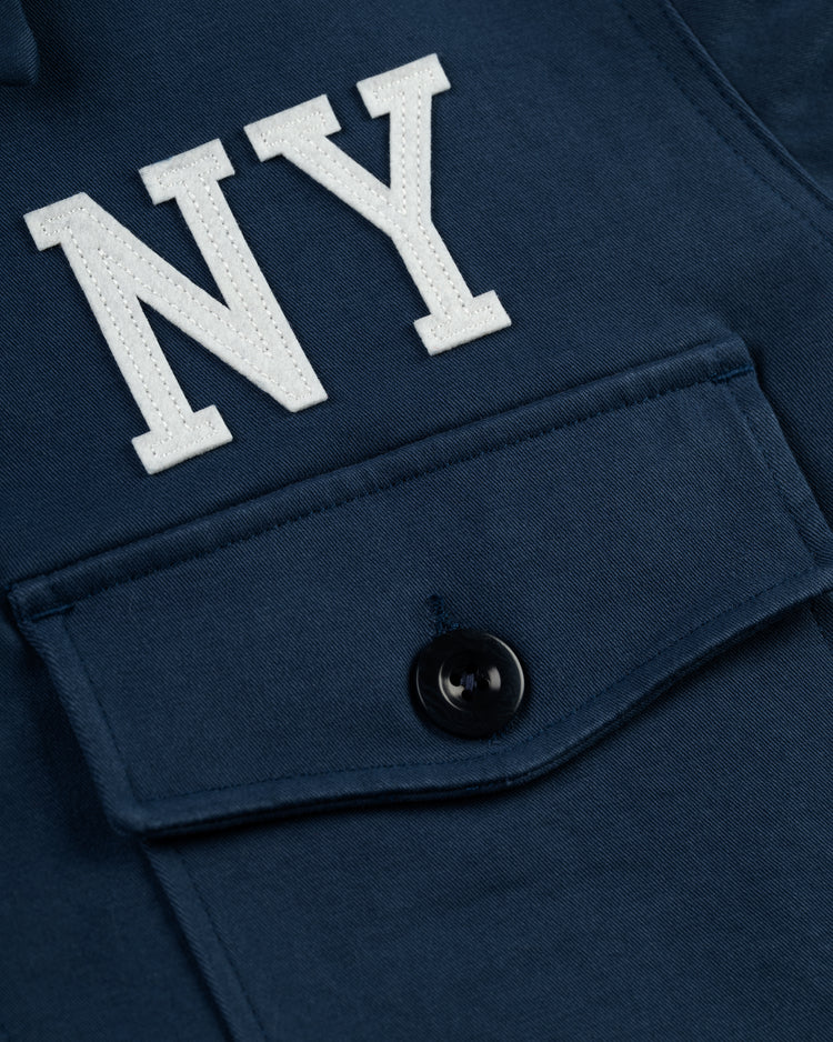 Close-up of the Ebbets Field Cotton Grounds Crew Jacket by Ebbets Field Flannels, featuring a navy blue cotton fabric, buttoned pocket, and bold white NY stitching—an ideal sporty addition to your spring collection.