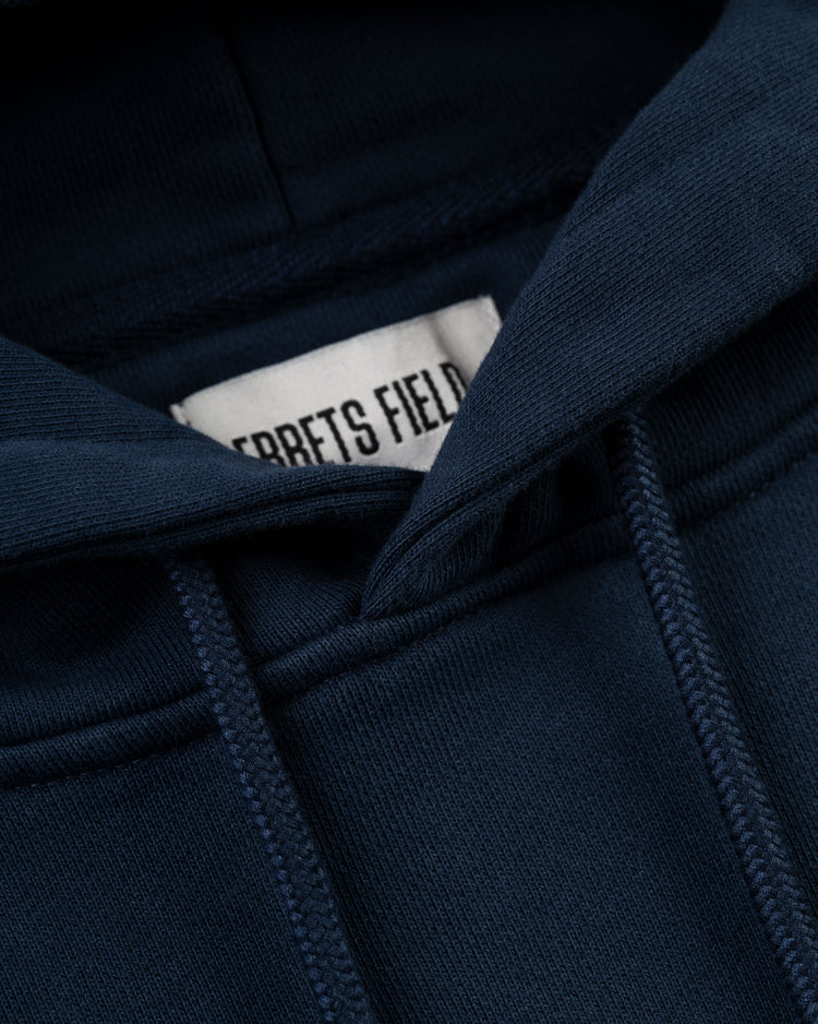 Close-up of the Ebbets Field Flannels Ebbets Chest Logo Heavyweight Cotton Terry Pullover Hoodie in navy, showing the hood, drawstrings, detailed stitching, and a partially visible white label.