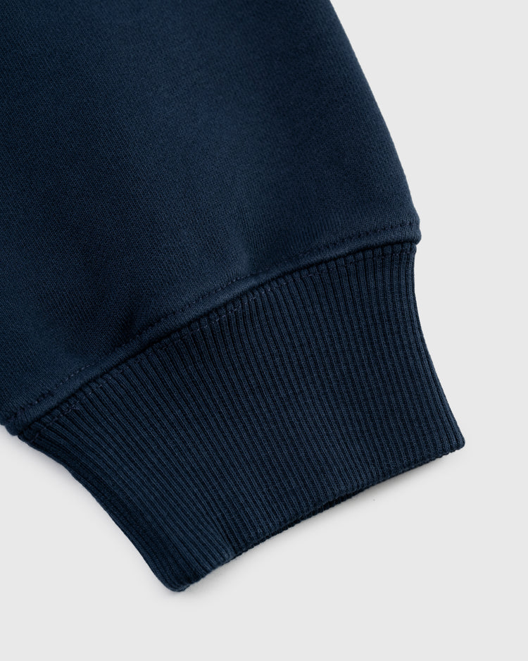 Close-up of the cuff of the Ebbets Field Flannels Ebbets Chest Logo Heavyweight Cotton Terry Pullover Hoodie in navy, highlighting ribbed knit fabric and neat stitching against a light gray background.