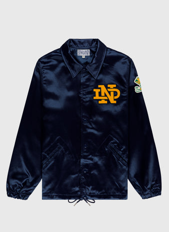 The EFF University of Notre Dame Satin Windbreaker Jacket is a shiny navy blue coach’s style featuring a yellow ND chest logo, colorful left sleeve patch, collar, snap buttons, two front pockets, and hem drawstrings.