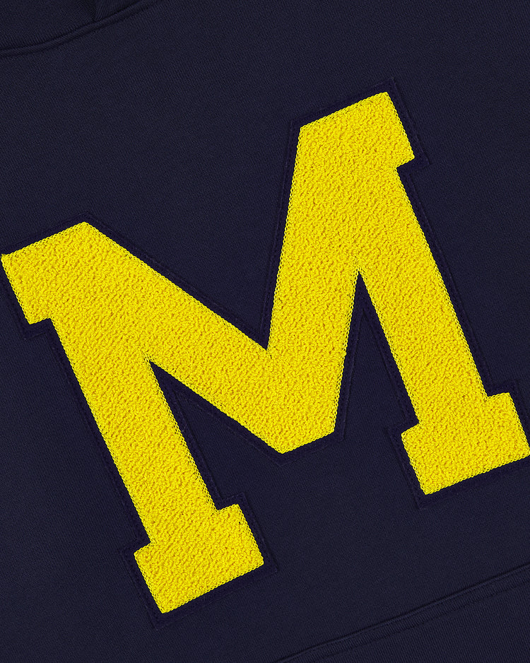 The Ebbets Field MICHIGAN HOODIE NAVY features a large, textured yellow letter M on a dark blue background.