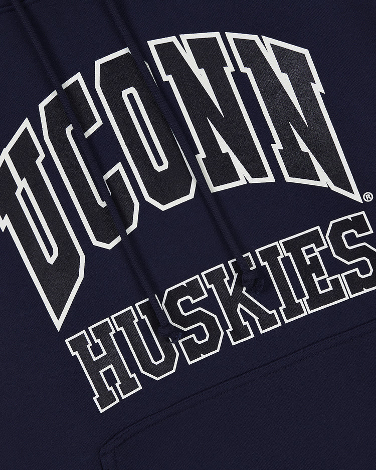 The UCONN HOODIE NAVY by Ebbets Field features bold white and black outlined UCONN above HUSKIES in a collegiate font on navy, plus visible drawstrings.