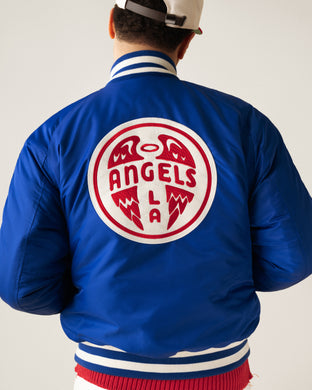 A person wearing a blue varsity jacket with white and red trim. The back features a large circular patch with red text reading Angels LA and a stylized angel wing design. The person’s face is not visible.