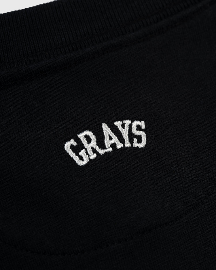 Close-up of the Ebbets Field Flannels Homestead Grays Embroidered G Long Sleeve Pocket Tee, featuring classic black fabric and white GRAYS embroidery—a tribute to Negro Leagues legend Josh Gibson and the Homestead Grays.