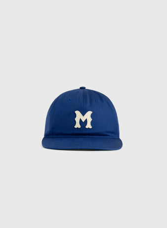 The Jackie Robinson Day Montreal Royals ‘M’ Cotton Twill Ballcap by Ebbets Field features a blue cap with a white stylized M on the front, shown against a plain light gray background.