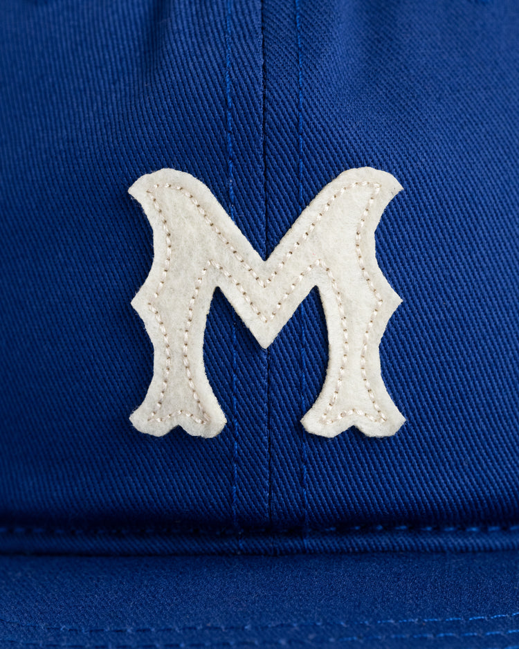 A close-up of the Ebbets Field Jackie Robinson Day Montreal Royals ‘M’ Cotton Twill Ballcap, featuring a white, stylized letter M stitched on the front.