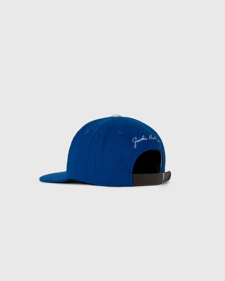 The EFF Jackie Robinson Day Commemorative Wool Ballcap is shown from the back in blue, with white cursive text near the opening and an adjustable black strap, styled in a classic Ebbets Field design against a light gray background.