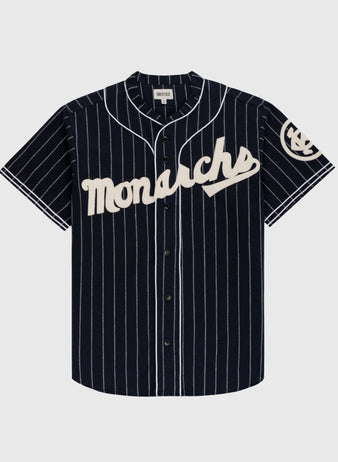 The Ebbets Field Kansas City Monarchs 1924 Authentic Wool Road Baseball Jersey features navy wool with white pinstripes, Monarchs script across the chest, and a classic Negro Leagues-inspired circular logo on the left sleeve.