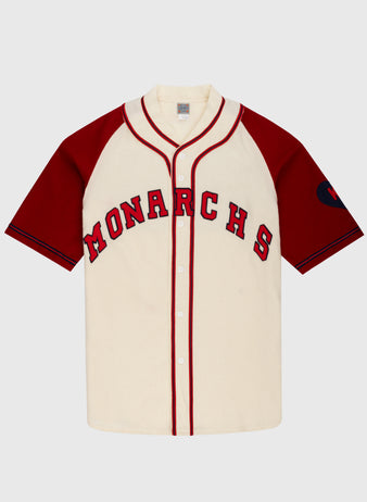 The Ebbets Field Kansas City Monarchs 1942 Authentic Wool Home Baseball Jersey features a cream body with red sleeves and piping, MONARCHS across the chest, and a left sleeve patch honoring Negro Leagues Baseball heritage.