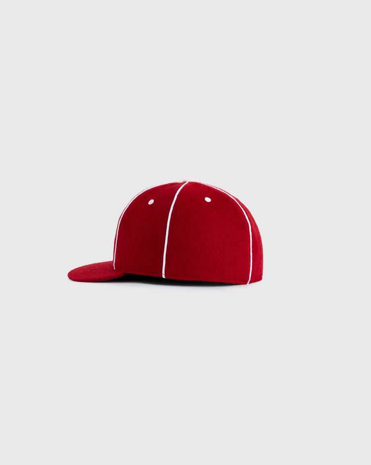 The EFF Hollywood Stars 1940 Authentic Wool Ballcap, shown from the side on a light gray background, features red wool with white stitching and a flat brim. It’s a faithful reproduction of the classic Pacific Coast League style.