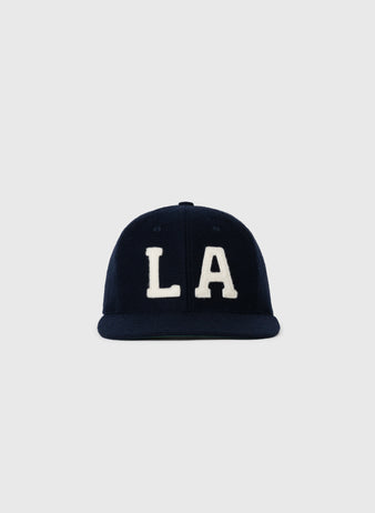 The EFF Los Angeles (PCL) 1949 Authentic Wool Ballcap is a navy blue cap featuring bold white “LA” letters, inspired by the Pacific Coast League Angels, shown against a plain light gray background.
