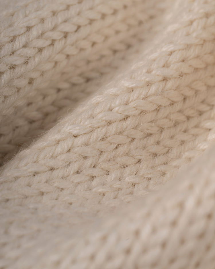 Close-up of beige knitted fabric with a textured, woven pattern reminiscent of vintage MLB style, as seen on the Atlanta Braves 1974 Wool Shawl Collar Sweater by Ebbets Field Flannels. Soft fibers evoke a classic, cozy appearance.