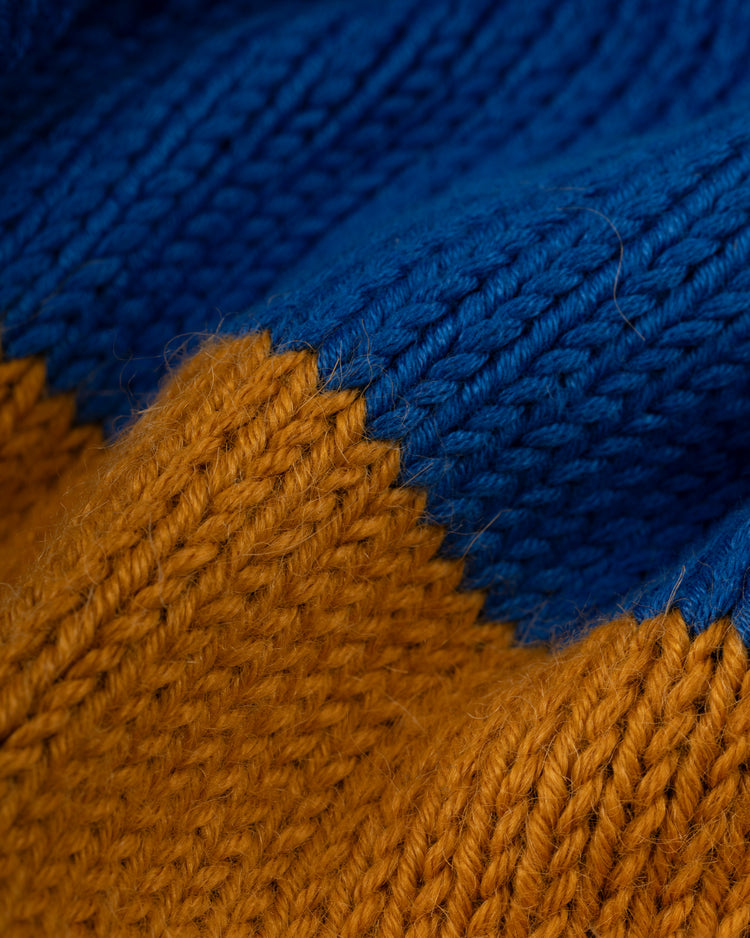 Close-up of the Ebbets Field Flannels Seattle Pilots 1969 Wool Shawl Collar Sweater, featuring vibrant blue over mustard yellow with a visible seam. Textured yarn and classic stitches evoke replica on-field baseball sweaters.