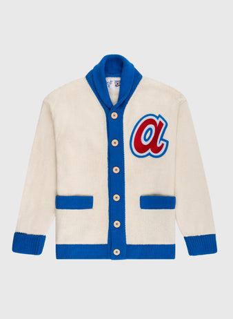 The Atlanta Braves 1974 Wool Shawl Collar Sweater by Ebbets Field Flannels is cream with blue trim, blue cuffs, two blue front pockets, tan buttons, and a large red and blue letter A patch inspired by vintage MLB and Braves styles.