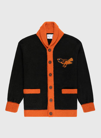 The Ebbets Field Flannels Baltimore Orioles 1964-65 Wool Shawl Collar Sweater is black with orange trim, cuffs, and pockets. It features an orange bird on the left chest, brown buttons, and a vintage-inspired shawl-collar design.