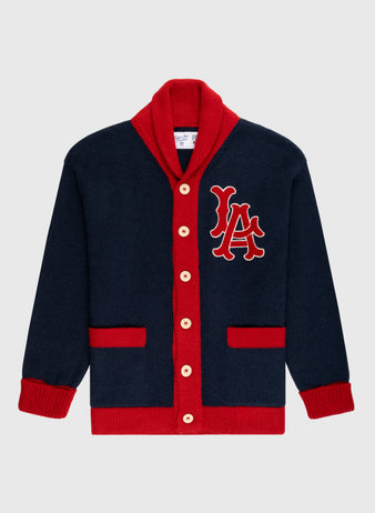 The Ebbets Field Flannels LA Angels 1961-65 Wool Shawl Collar Sweater is navy blue with red trim, cuffs, buttons, and pockets. Large red and white LA letters are embroidered on the left chest, inspired by vintage on-field sweaters.